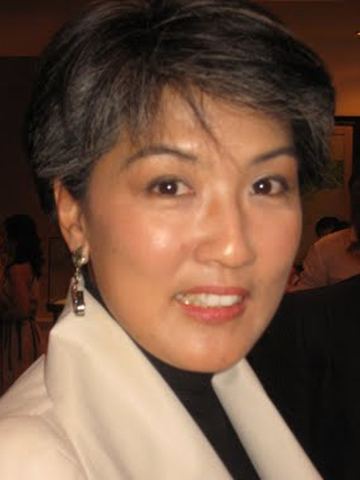 Irene Marcos smiling with short hair and wearing a black turtle blouse under a white coat