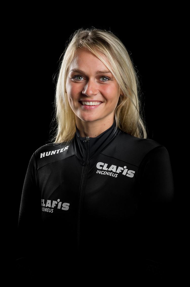Irene Schouten smiling in a black background and having a blonde hair and wearing a black jacket with white prints
