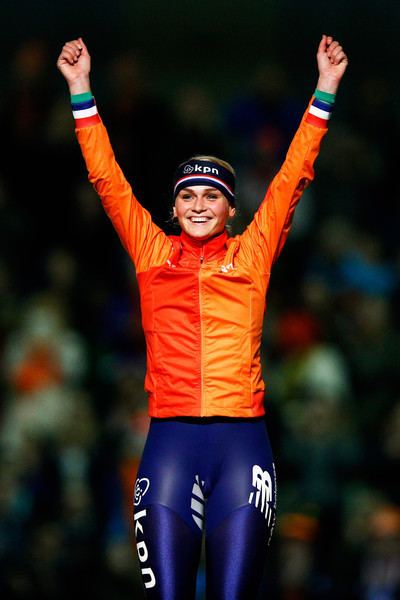 Irene Schouten looking happy and raising both of her hands with closed fists and wearing an orange jacket with red, white, blue, and green color stripes, blue leggings with white prints, and a blue headband with red and white stripes and print