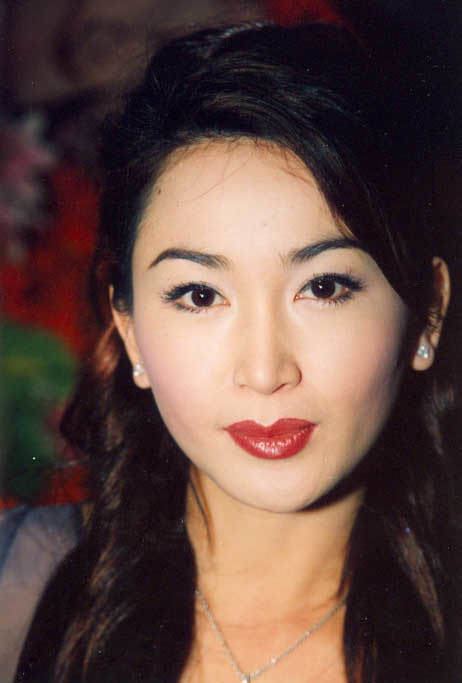 Irene Wan with a tight-lipped smile while wearing a blue blouse, necklace, and earrings