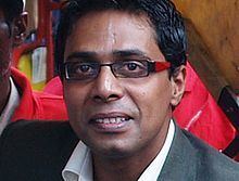 Irfan Alam smiling while wearing eyeglasses, gray coat, and white long sleeves