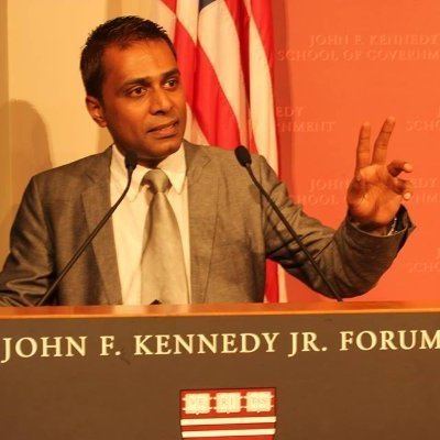 Irfan Alam giving a speech while wearing a gray coat, white long sleeves, and gray necktie