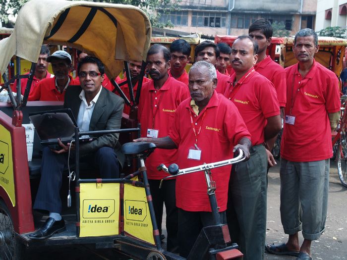 Irfan Alam riding in the rickshaw and beside him are the rickshaw pullers wearing a red polo shirt and pants