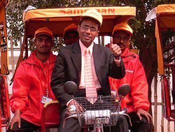 Irfan Alam smiling while riding in the rickshaw and behind him are the three men wearing a red jacket and cap