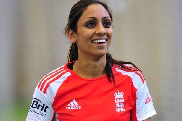 Isa Guha wearing white and orange shirt while smiling