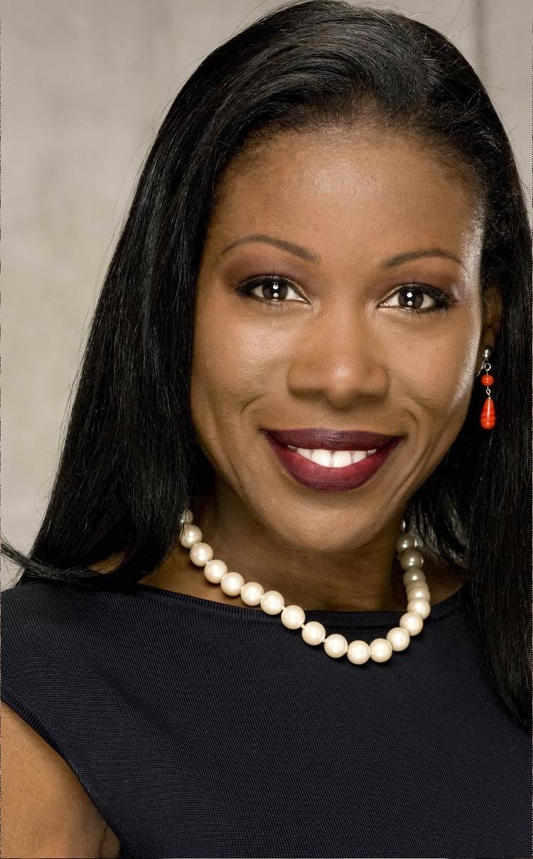 Isabel Wilkerson smiling while wearing a black blouse, pearl necklace, and red earrings