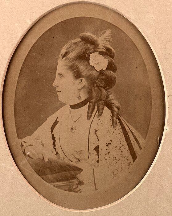 Isabella Eugénie Boyer looking serious on a side view inside an oval frame with curly hair and a flower pinned on it while wearing a white dress, dangling earrings, necklace, and choker