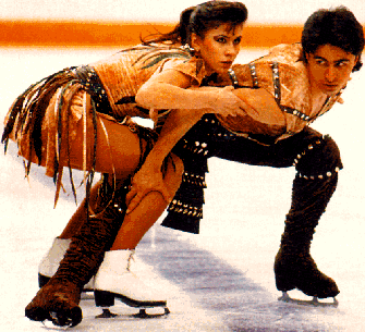 Isabelle and Paul Duchesnay are dancing on ice with a fierce look. Isabelle is wearing a black and brown dress and white skating shoes while Paul is wearing a brown sleeveless polo, black pants, and black skating shoes