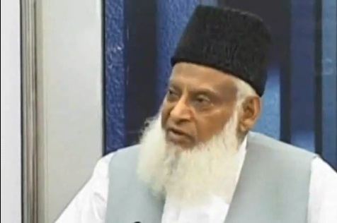 Israr Ahmed with a long white beard, wearing a black hat and a white and gray thobe.