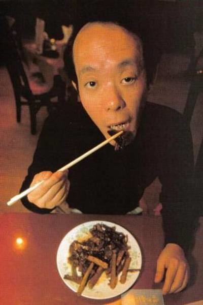Issei Sagawa with a serious face while eating and wearing a black long sleeve shirt.