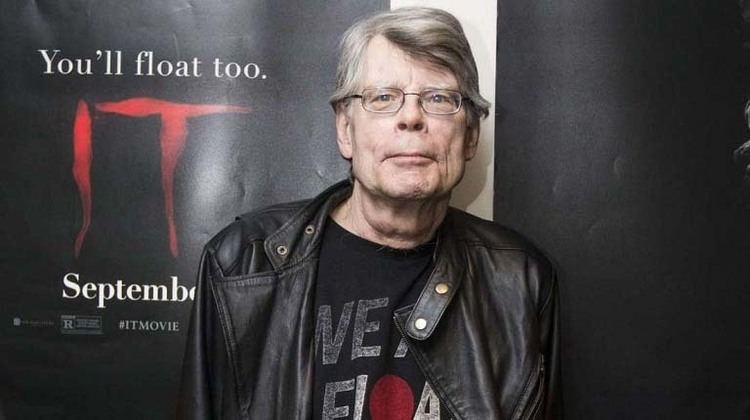 Stephen King wearing a black leather jacket, black printed shirt, and eyeglasses