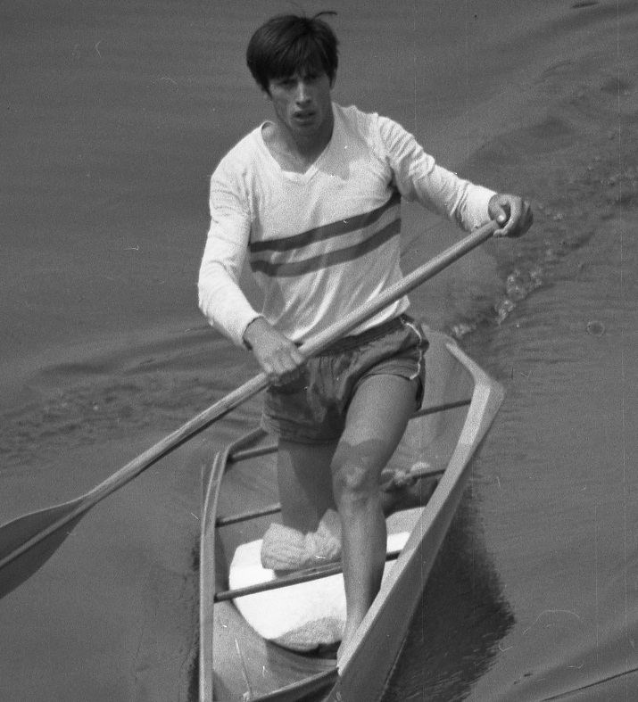 Ivan Patzaichin riding in the canoe while wearing a long sleeve shirt and shorts