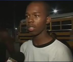 Jabbar Gibson being interviewed in Houston, with the bus he drove visible behind him while he is wearing a black and white t-shirt