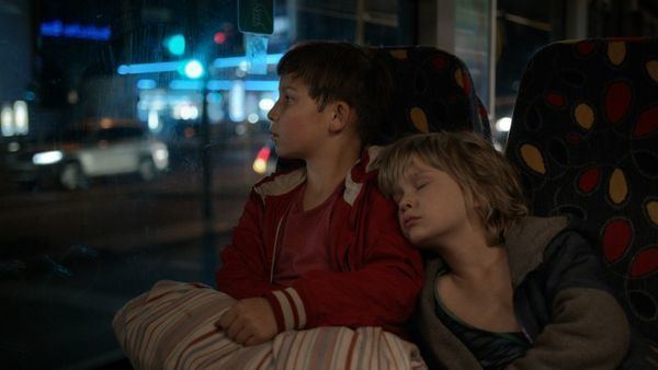 In the movie scene of Jack (2014 film),  on the left is Ivo Pietzcker is serious, looking to his right window, holding a big striped cloth, sitting in the bus has brown hair wearing a shirt under a red hoodie jacket, at the right Georg Arms is sleeping, laying on Ivo Pietzcker left chest, sitting in a bus has blonde hair, wearing a black shirt under a gray jacket.