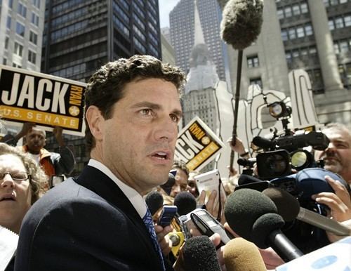 Jack Ryan is surrounded by reporters while being interviewed and he is wearing a black coat, white long sleeves, and blue necktie