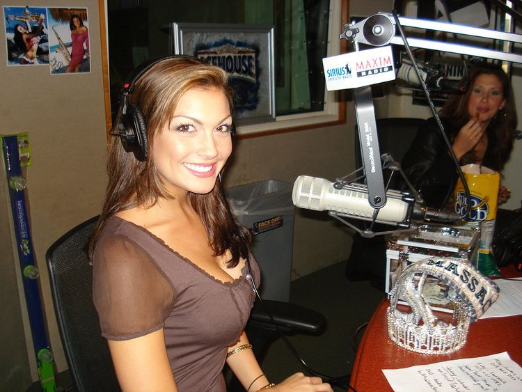 Jackie Bruno smiling while sitting on the chair at the Maxim radio studio while wearing a brown blouse and headset