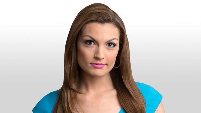 Jackie Bruno with a tight-lipped smile while wearing a sky blue blouse and hoop earrings