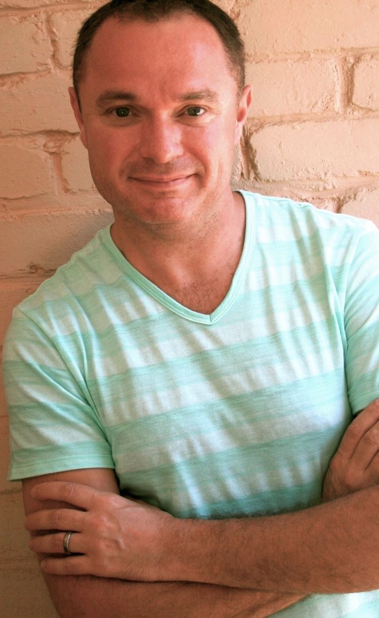 Jaco Jacobs smiling closed mouth with his arms crossed and wearing a light green striped shirt.