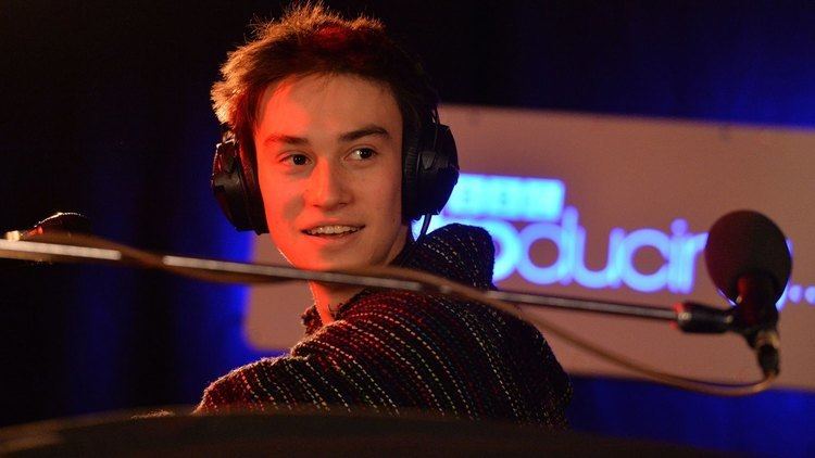Jacob Collier smiling and wearing headphones.