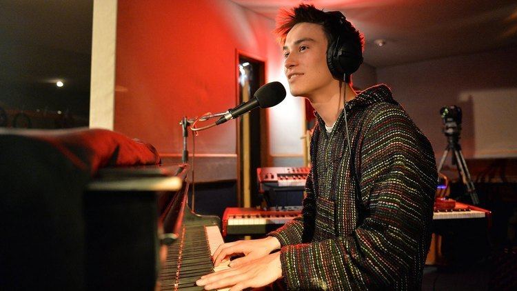 Jacob Collier wearing headphones while playing the piano with a microphone in front of him.