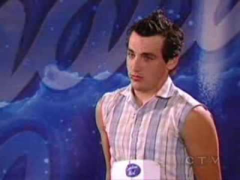 In the Canadian Idol Jacob Hoggard is serious, has black in mohawk hair, wearing a plaid top.