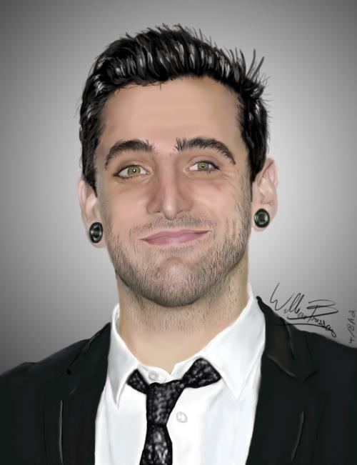 Jacob Hoggard is smiling, has black hair brown eyes, a beard and a mustache, wearing black earrings on both ears, white long sleeves, and a black necktie under a black suit.