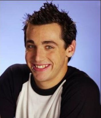 Jacob Hoggard is smiling, has black hair piercing in his mouth, wearing a black and white shirt.