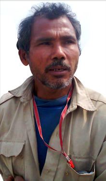 Jadav Payeng looking afar with a serious face, mustache, and beard while wearing a red id lace and blue shirt under a beige jacket
