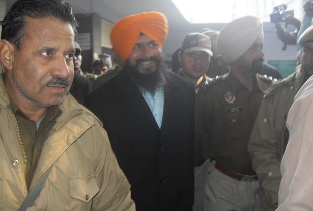 Jagtar Singh Hawara smiling with a beard and mustache and surrounded by officials, wearing a white shirt under a black coat and an orange turban