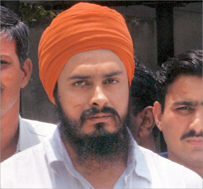 Jagtar Singh Hawara looking serious with a beard and mustache with other men standing beside him, wearing a white shirt and an orange turban