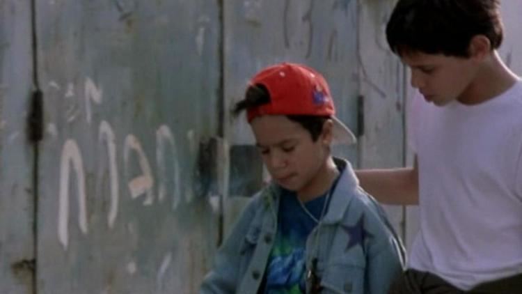 Saúl Fonseca wearing a white t-shirt and Sandro Silva wearing a red cap, long sleeves, and t-shirt in a scene from the 1999 film, Jaime