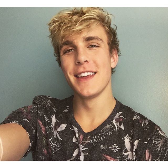 Jake Paul smiling while wearing a black, white, and pink printed t-shirt