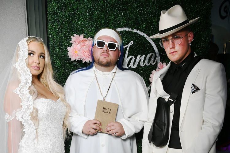 On the left, Tana Mongeau wearing a veil and wedding gown, a priest at the center, and Jake Paul on the left wearing a hat, white coat, and black long sleeves
