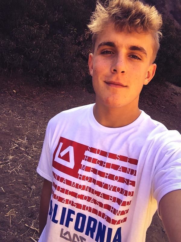 Jake Paul with a tight-lipped smile while wearing a white, red, and blue printed t-shirt