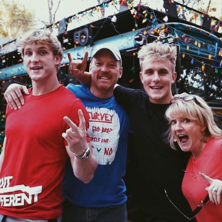 Logan Paul, Gregory Allan Paul, Jake Paul, and Pamela Ann Stepnick are smiling and behind them is a car surrounded by colorful light bulbs