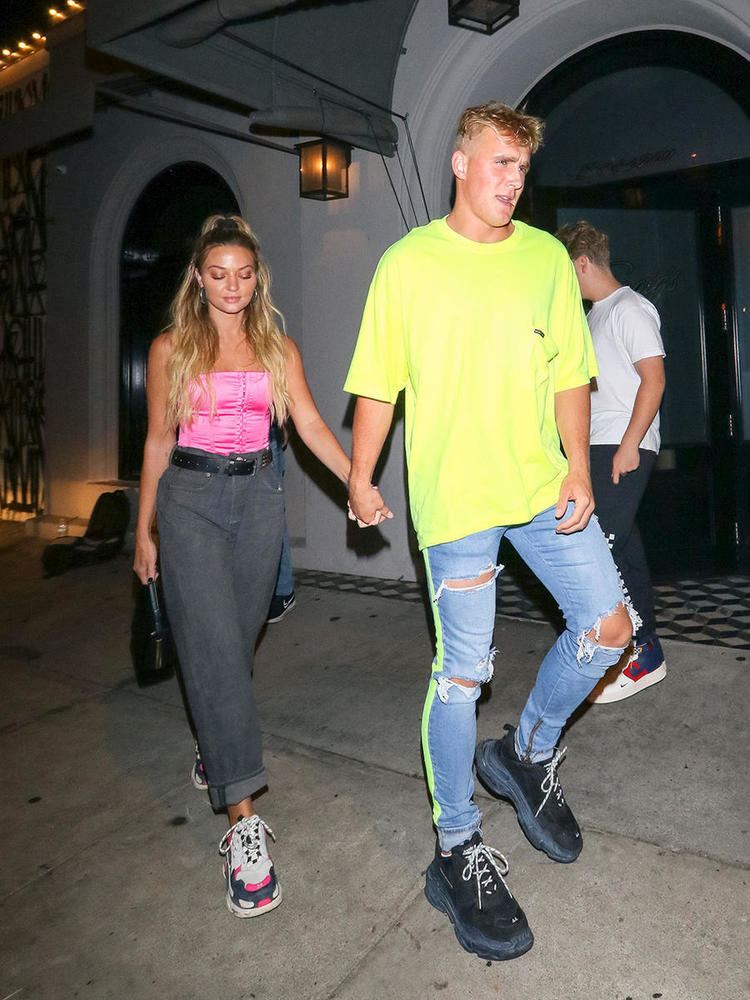 Erika Costell and Jake Paul walking hand in hand while Jake is wearing a yellow t-shirt and denim pants and Erika wearing a pink top and gray pants