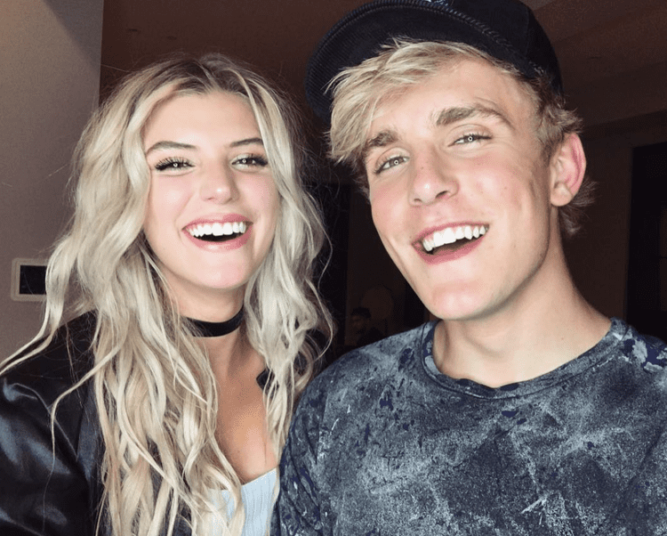 Alissa Violet and Jake Paul are smiling while Jake is wearing a gray t-shirt and Alissa wearing a black blazer, white blouse, and choker