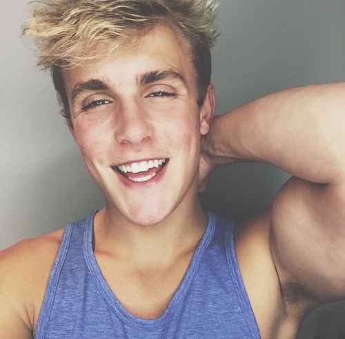 Jake Paul with a big smile while hand is on his neck and wearing a blue sando
