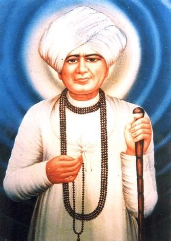 Jalaram Jay holding a wooden stick and a necklace while wearing a white turban, white long sleeves, and a black beaded necklace