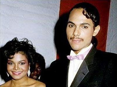 Janet Jackson smiling with James DeBarge, wearing a black coat, white long sleeves, and violet bow tie