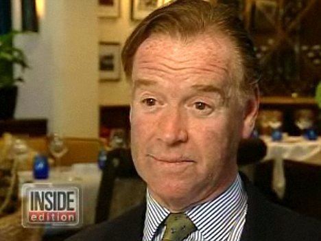 In the INSIDE edition scene, a room with a long table with glasses on top, and brown chairs, in front, James Hewitt is serious, sitting, has brown hair wearing a white striped polo and olive green necktie under a black coat.