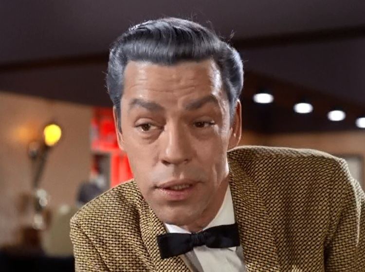 James Lanphier talking to someone while wearing a black and yellow coat, white long sleeves, and black bow tie in a scene from the 1963 tv series, The Fugitive