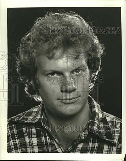 James Stephens smiling closed mouth with thick hair and wearing a checkered polo shirt.