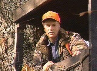 Jameson Parker wearing a brown jacket, orange hat, and blue long sleeves