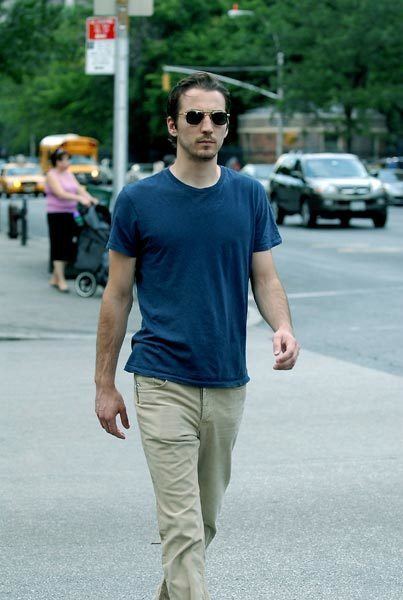 Jamie Johnson walking on the street while wearing a blue t-shirt, khaki pants, and sunglasses