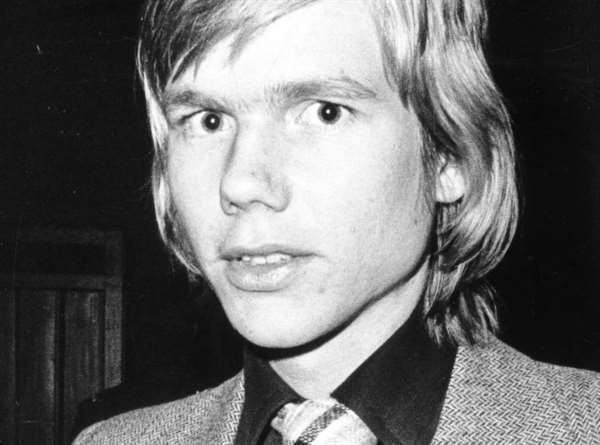 Jan-Erik Olsson looks shocked with his blonde short hair wearing a black polo with a necktie under a gray coat in an old photograph