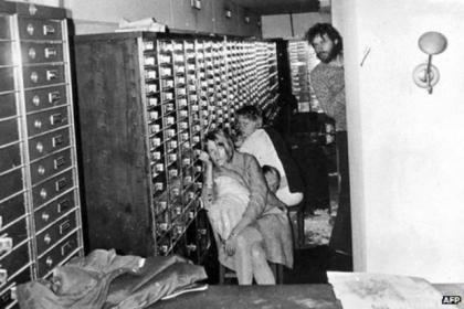 Jan-Erik Olsson's captors, 2 ladies sitting while leaning on a cabinet, wearing long sleeves, and 1 man standing with beard and mustache wearing a polo long sleeve and pants inside at the Kreditbanken bank during their 121-hour ordeal in 1973