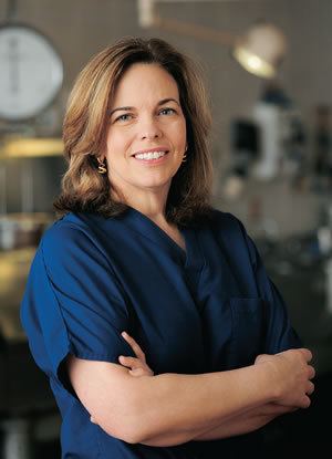 Jan Garavaglia smiling, with blonde hair, wearing earrings, and a blue shirt.