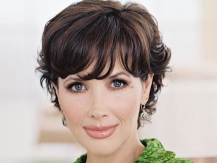Janine Turner smiling with a short hair, dangling earrings wearing a green blouse