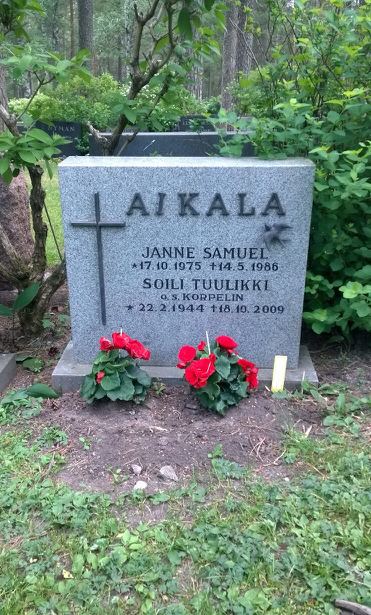 A tombstone of Janne Samuel has his name, birth date (17.10.1975), and death date (14.5.1986), below his name, is Soili Tuulikki’s name on the tombstone, and birth date (22.2.1944), and death date (18.10.2009) in Karsamaki, Turku Municipality, Finland Proper, Finland with a cross, flowers, and candles.